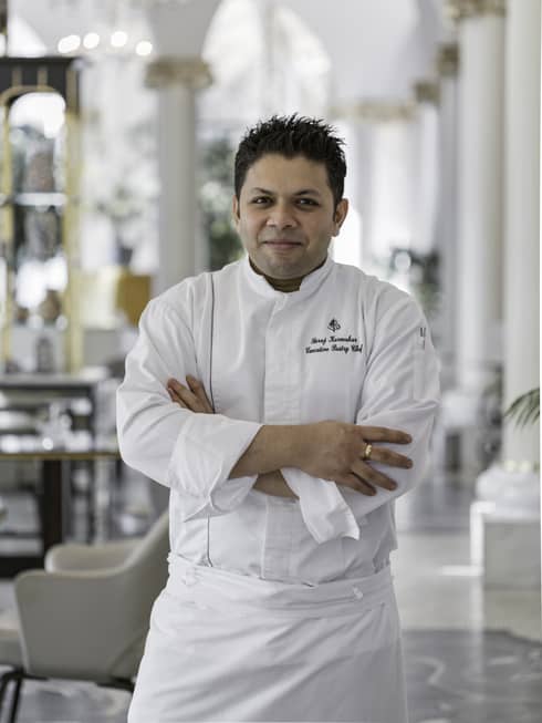 Chef Suraj standing, arms folder, in white chef?s coat and apron