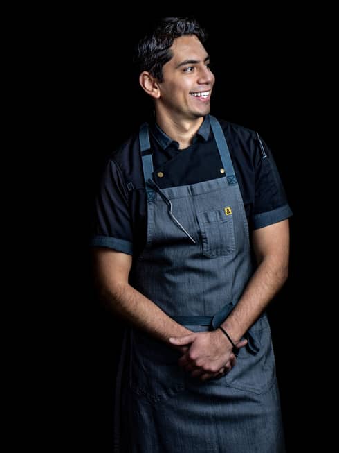 A chef in a dark grey apron on a black background.