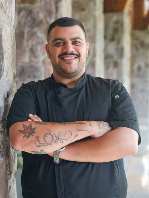 A chef in a black chefs coat standing outside.