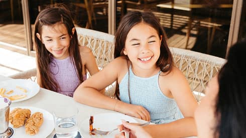 Three guests sitting at an outdoor dining table with floor-to-ceiling windows in the background