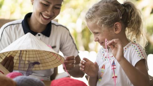 Hotel staff helps young girl thread string on traditional hat