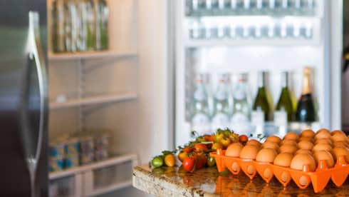 Smiling man holds green bottle in front of open fridge, fresh eggs on counter