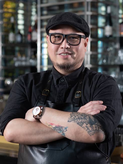 A bartender with a dark hat, apron and tattoos.