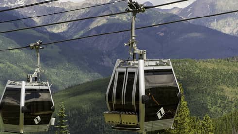 Two gondolas travelling over a forested area.