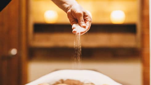 Closeup of a masseuse giving a guest a Himalayan salts treatment in a dimly lit spa