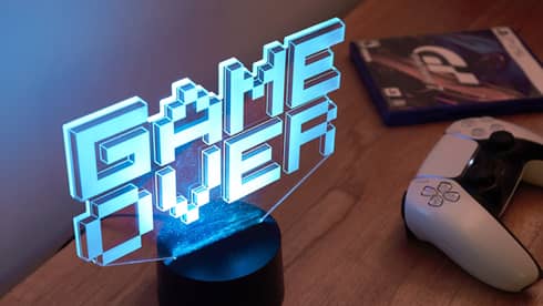 Neon "Game Over" sign in blue letters lights up a wooden table with a white gaming console on it
