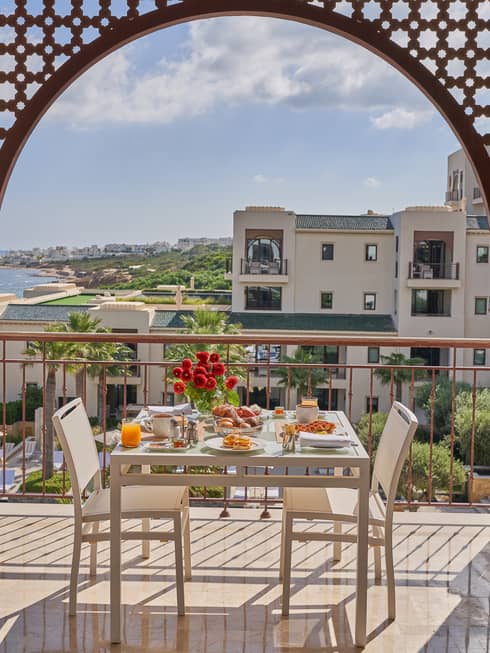 Outdoor table with flowers and elaborate breakfast spread on a balcony overlooking Tunis and water
