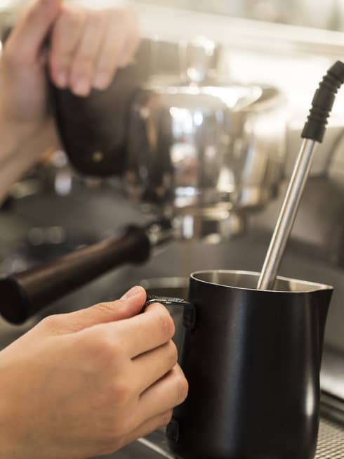 Close-up of hands with milk steamer at espresso machine
