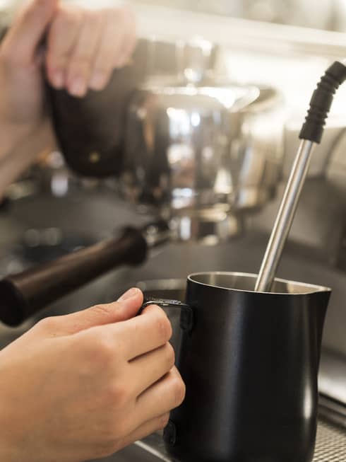 Close-up of hands with milk steamer at espresso machine