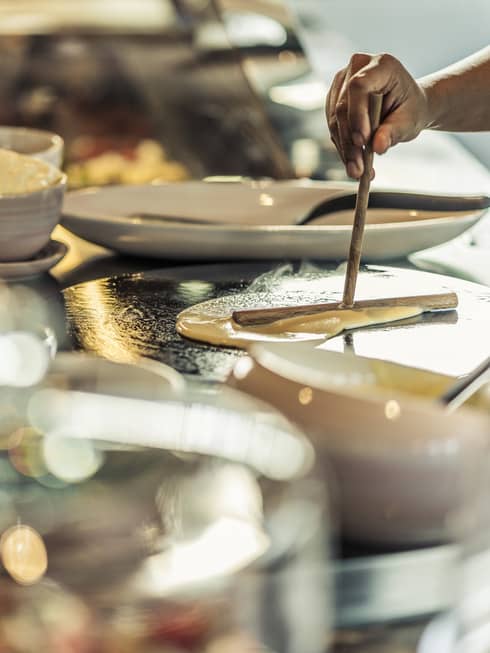 A chef pours crepe batter onto a hot plate near the crepe buffet