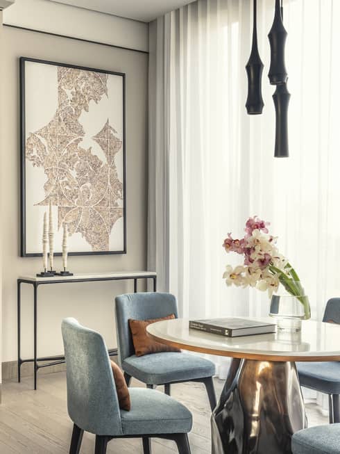 Modern dining room with light blue chairs, a round white table, a vase of orchids and a small bar area with a coffee machine and liquor bottles.