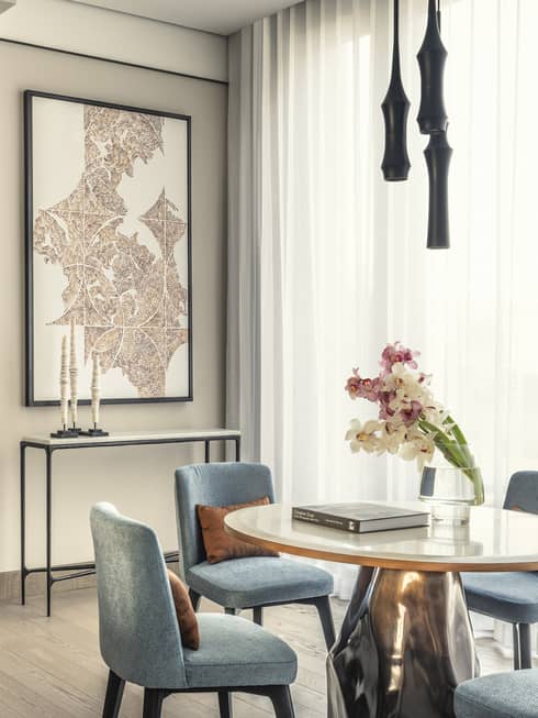 Modern dining room with light blue chairs, a round white table, a vase of orchids and a small bar area with a coffee machine and liquor bottles.