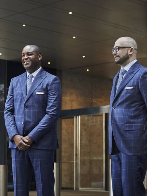 Two men in suits waiting outside of a Four Seasons Hotel entrance.