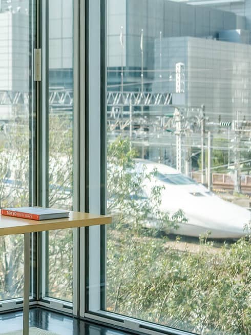 Modern seating area with a table set for tea and a vase with white flowers, overlooking large windows with a view of a high-speed train passing