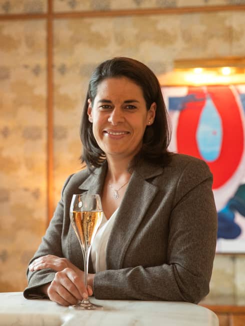 Sommelier Claudia Gozalbes in brown blazer, sitting and smiling while holding a glass of white wine