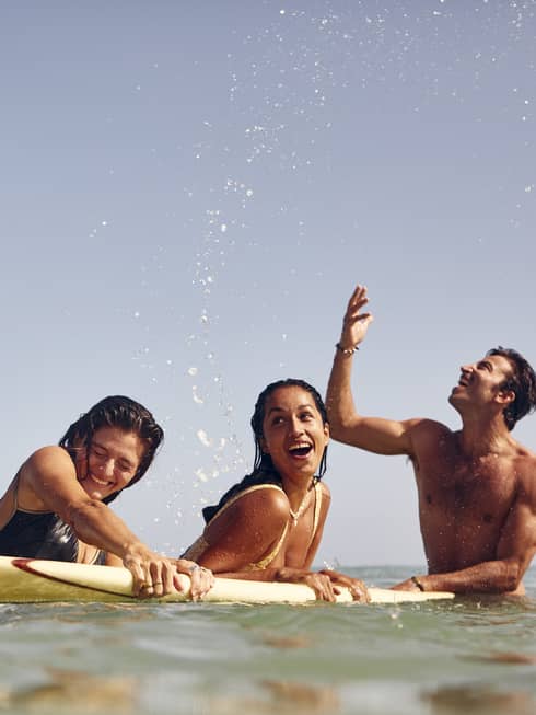 Two women and a man holding onto a surfboard in the ocean.