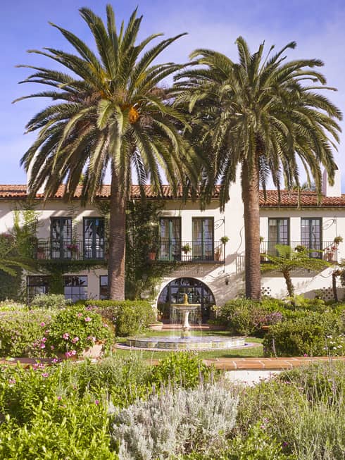 Fountain under palm trees in sunny garden in front of Four Seasons Hotel villa-style building