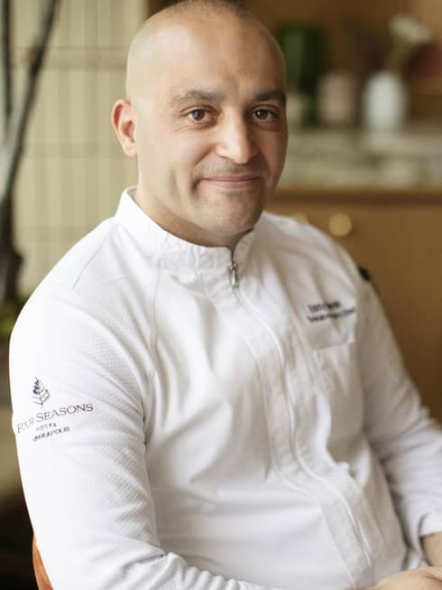 Chef Eddy Dhenin sitting in the kitchen wearing a chefs coat.