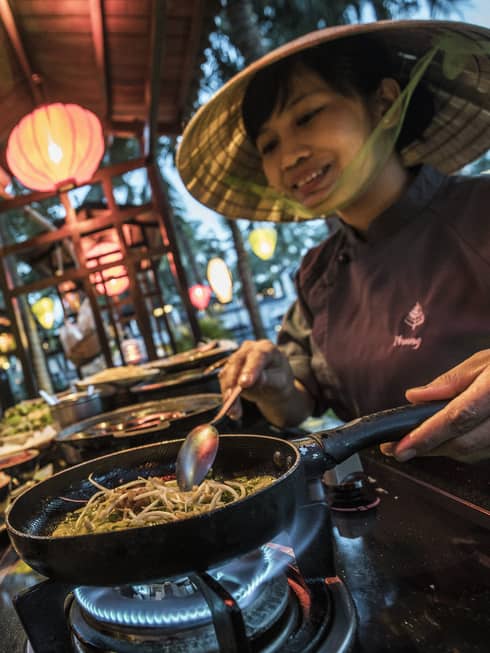 Chef cooks street food noodles in traditional Vietnamese rice hat