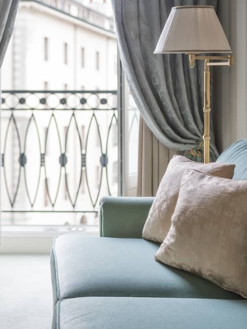 Close-up of blue sofa, two cream accent pillows, white and gold lamp, sunny French balcony in background