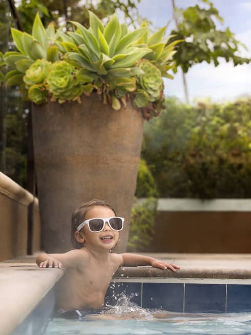 Child wearing sunglasses sitting in the pool.