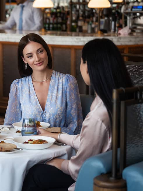 Two women sitting at a round dining table in the center of a restaurant