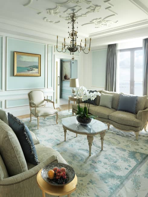 Presidential Suite sunny living room with two elegant sofas, coffee table under small chandelier by window, marble fireplace
