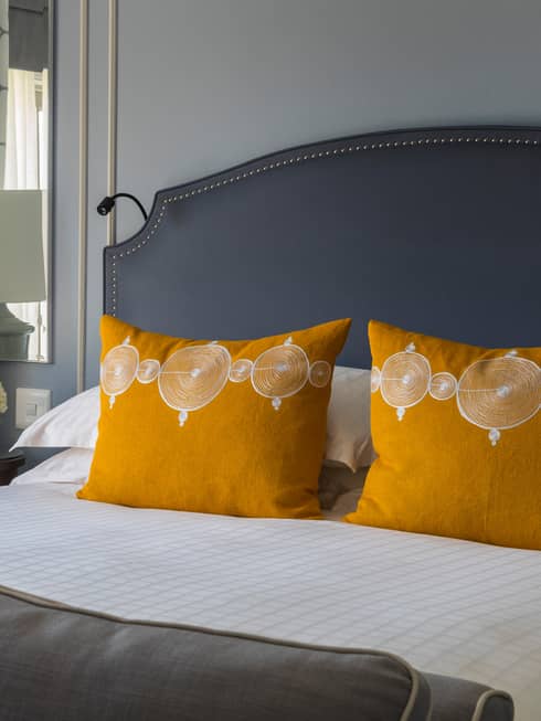 One Bedroom Suite bed with bright yellow accent pillows, white lamp on nightstand in front of mirror