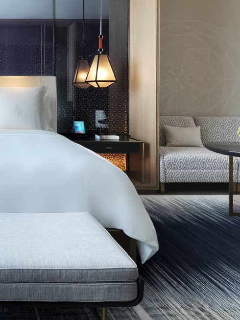 Close-up of modern upholstered chaise with rolled pillow at foot of hotel room bed with white linens