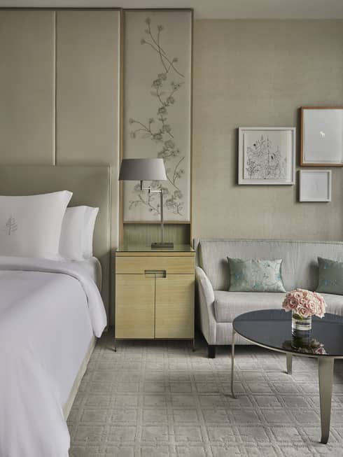 Guest room at Four Seasons Hotel Toronto, with light-coloured furniture, carpet, and walls. Glass coffee table with flowers.