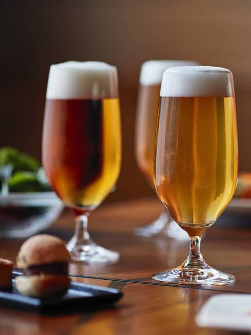 Four tall beer glasses filled with beer on a table with cheese, crackers and appetizers