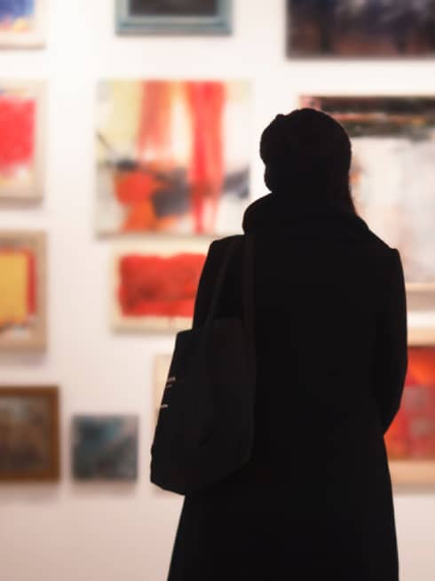 Silhouette of back of woman with hat bag looking at gallery wall with colourful art