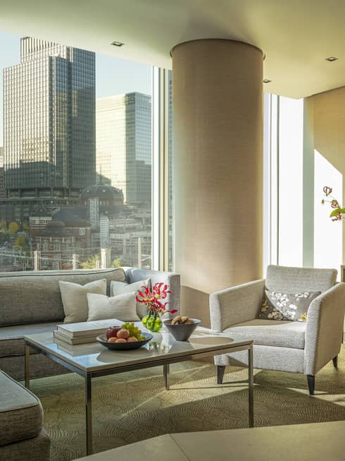 Four Seasons executive suite with gray sectional sofa, armchair, coffee table with fruit and flowers, large window with city view, TV and console table