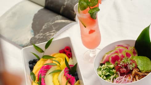 Fresh fruit and salad in white containers set on a day bed