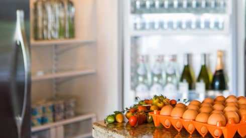 Smiling man holds green bottle in front of open fridge, fresh eggs on counter