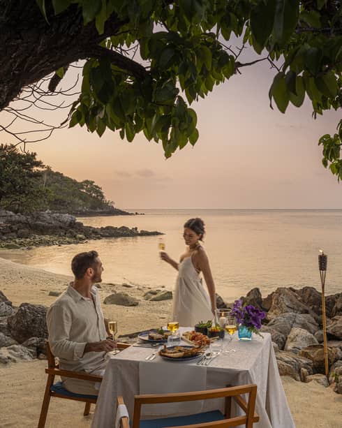 A beach dinner date at dusk, with a couple enjoying a serene seaside view.