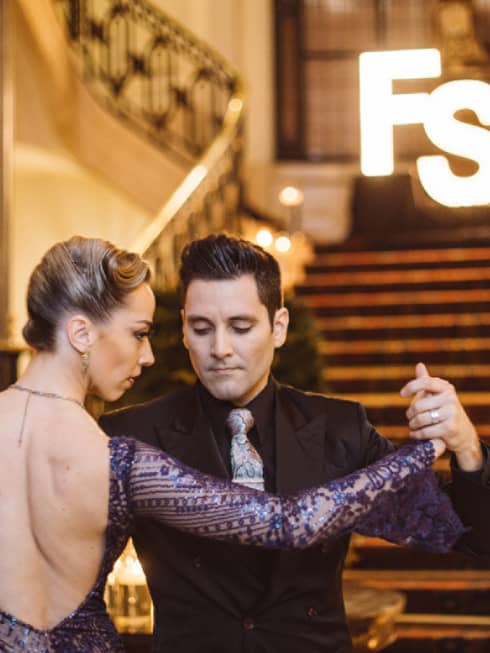 A man and woman tango dancing at the bottom of a wide red carpeting stairway