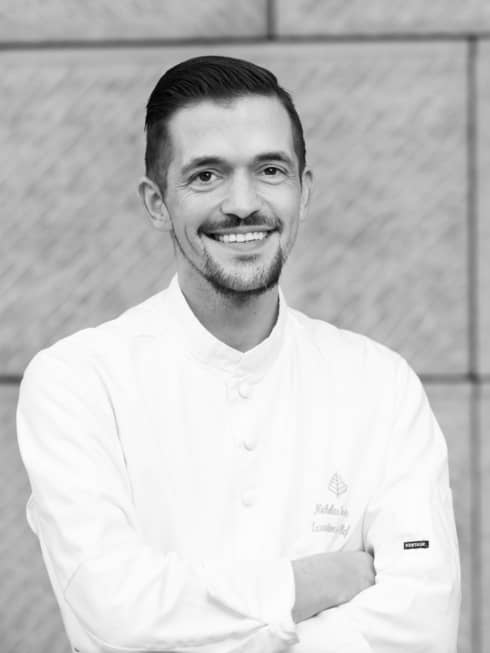 Executive Sous Chef Nicholas Trosien in white chef?s coat, smiling and standing with arms folded