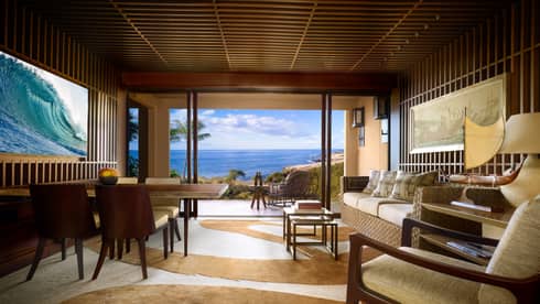 Teak panel wall with TV, wood dining table across from wicker sofa, swirl-patterned carpet