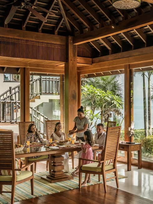 Butler serves family at long table in bright corner window dining room with windows