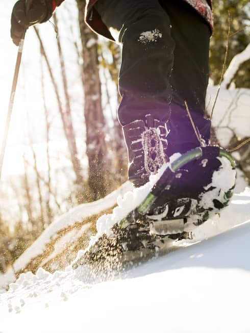 A person walking on snow using snow shoes and poles to help them walk.