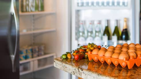 Smiling man holds green bottle in front of open fridge, fresh eggs on counter