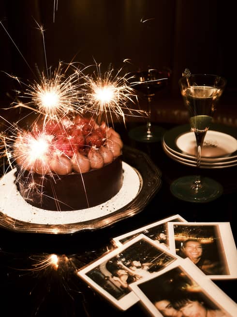 Sparkler candles in a chocolate cake and polaroid pictures nearby on a table