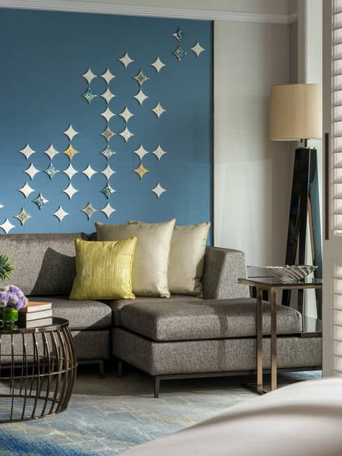 Gold pillows on grey sofa against blue wall with star-shaped Peranakan tile mural