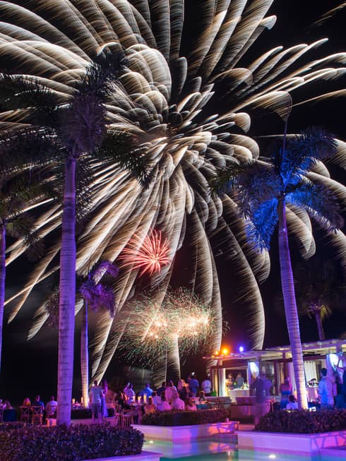 People around resort outdoor pool/bar watching fireworks in the night sky