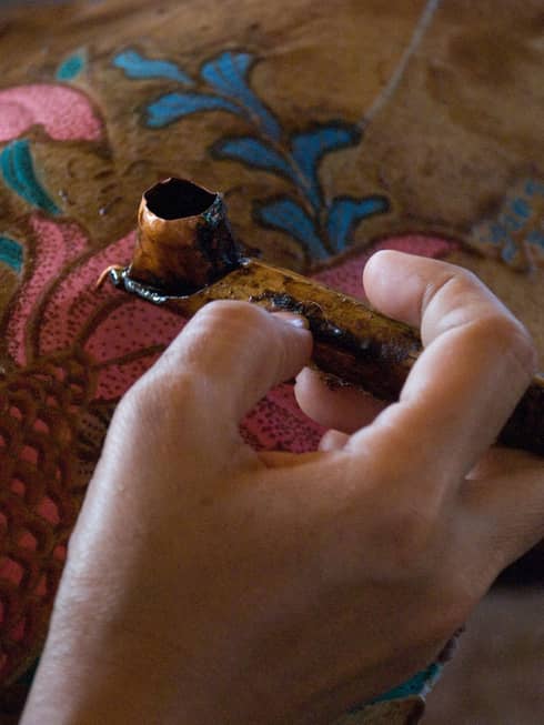 A hand holds a carved pipe above an intricately embroidered cloth