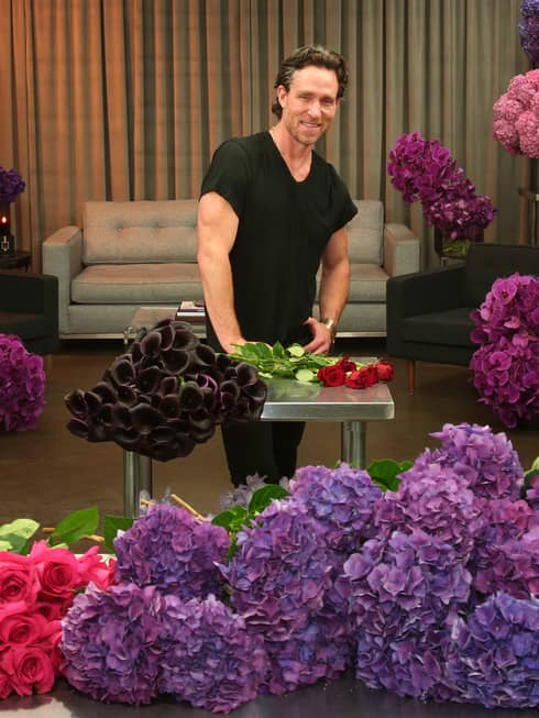 A man in a black shirt surrounded by red, purple and pink flowers.