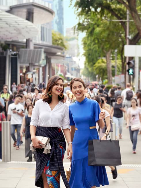 two well-dressed women carrying shopping bags and walking through a busy street in singapore