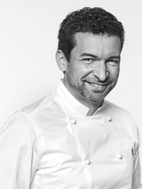 Guillaume Cabrol in white chef's coat, hands in pockets, smiling