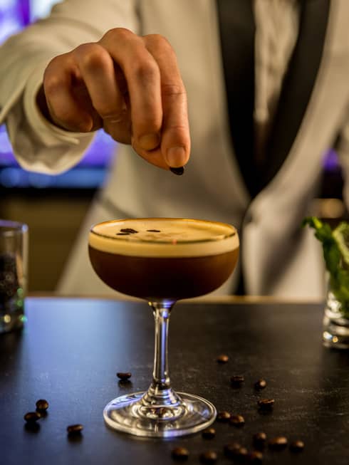 A bartender garnishing a dark cocktail with coffee beans.